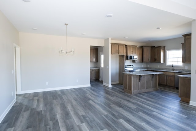 kitchen featuring baseboards, dark wood-style floors, a center island, stainless steel appliances, and a sink