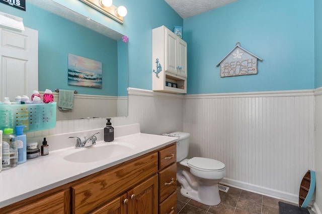 bathroom featuring tile patterned flooring, wainscoting, vanity, and toilet