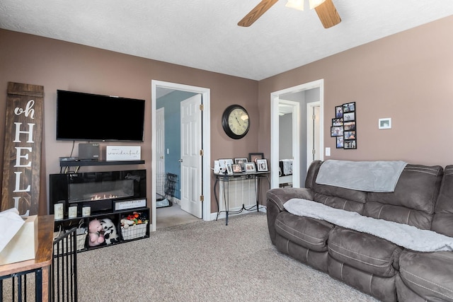 carpeted living room featuring a glass covered fireplace, ceiling fan, and a textured ceiling