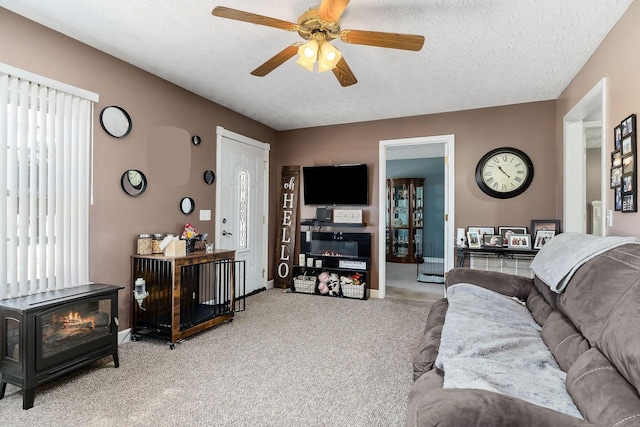 living room with light colored carpet, a ceiling fan, a wood stove, a textured ceiling, and baseboards