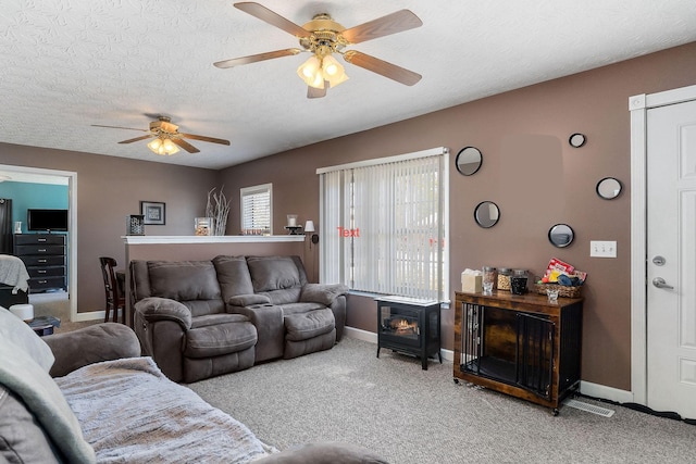 living area with a ceiling fan, a wood stove, carpet flooring, a textured ceiling, and baseboards