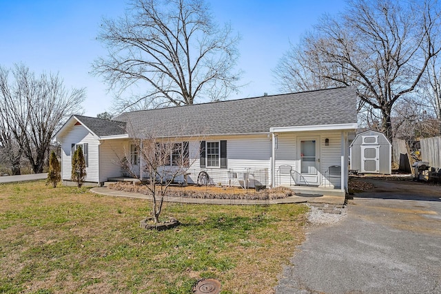 ranch-style home with a storage shed, a shingled roof, an outdoor structure, driveway, and a front yard