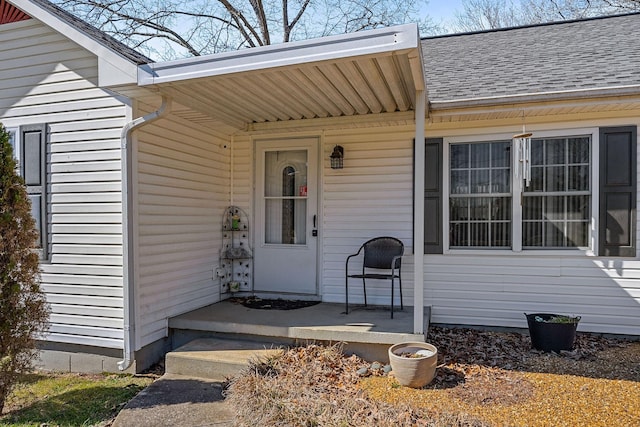 doorway to property featuring covered porch and roof with shingles