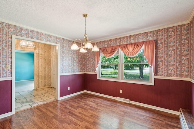 unfurnished dining area featuring wallpapered walls, visible vents, a wainscoted wall, a textured ceiling, and a chandelier