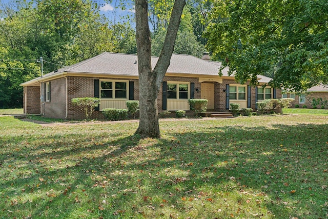 ranch-style home featuring roof with shingles, brick siding, a front lawn, and a chimney