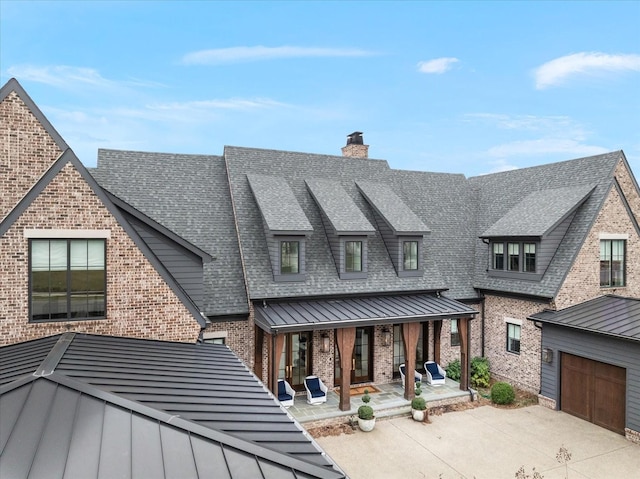 view of front facade with metal roof, brick siding, a shingled roof, concrete driveway, and a standing seam roof