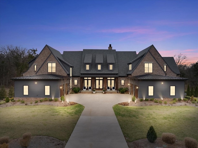 view of front of home featuring driveway, a standing seam roof, a lawn, and brick siding