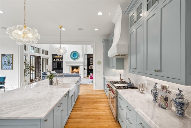 kitchen with a warm lit fireplace, open floor plan, stainless steel stove, premium range hood, and a sink