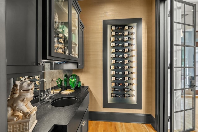 wine cellar featuring light wood-style flooring, wet bar, baseboards, and a sink