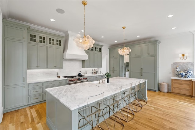 kitchen with light wood-type flooring, custom range hood, ornamental molding, and range with two ovens