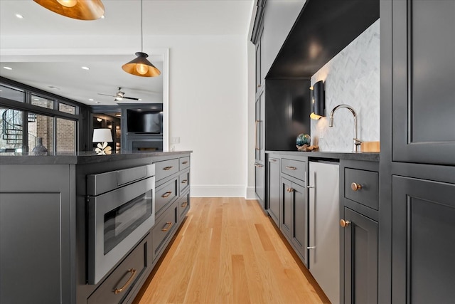 kitchen with dark countertops, stainless steel appliances, hanging light fixtures, and light wood-type flooring