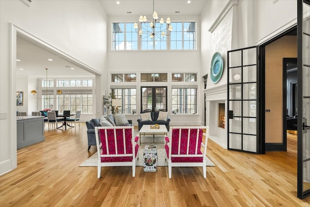 living area with light wood-type flooring, a towering ceiling, a notable chandelier, and french doors