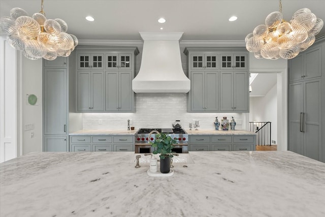 kitchen featuring a chandelier, premium range hood, high end range, and light stone countertops