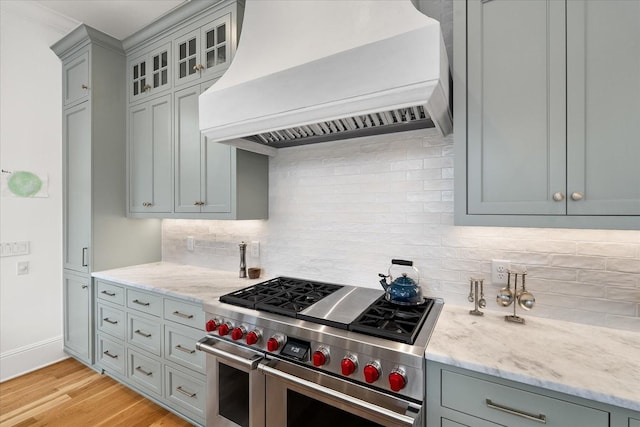 kitchen with range with two ovens, light stone counters, light wood finished floors, custom range hood, and backsplash