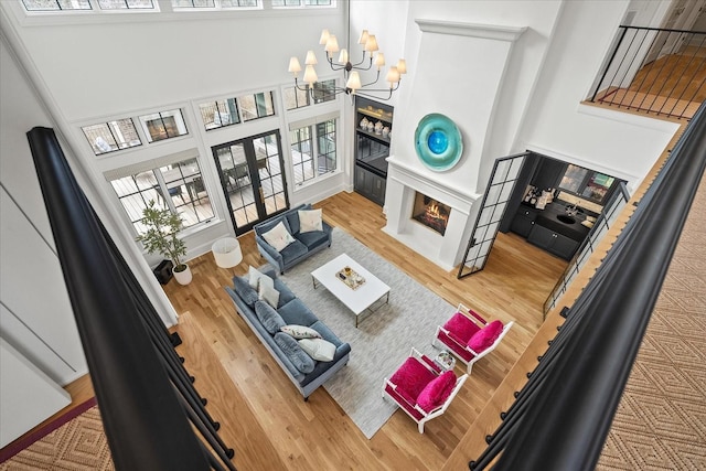 living area featuring a warm lit fireplace, a notable chandelier, wood finished floors, and french doors