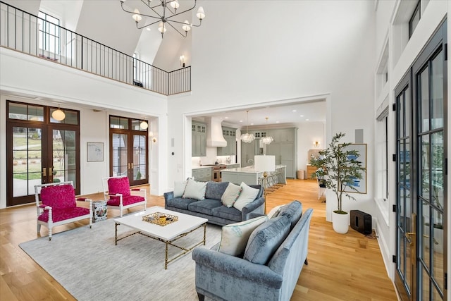 living room featuring light wood-style floors, french doors, a notable chandelier, and a high ceiling