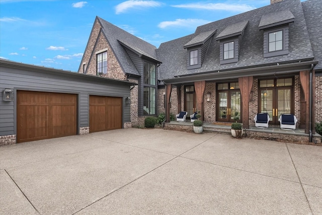 view of front of property featuring french doors, roof with shingles, brick siding, and driveway