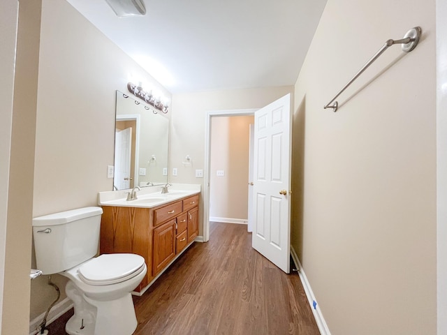 bathroom with double vanity, toilet, a sink, wood finished floors, and baseboards