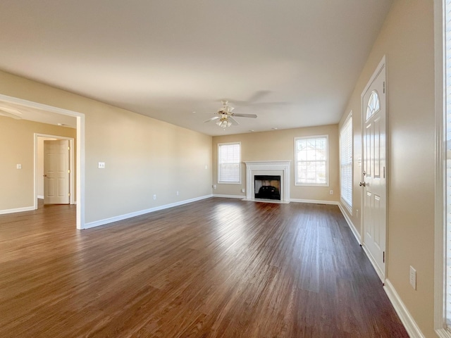 unfurnished living room with dark wood-style floors, a fireplace with flush hearth, baseboards, and a ceiling fan