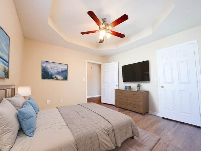 bedroom featuring ceiling fan, wood finished floors, a raised ceiling, and baseboards