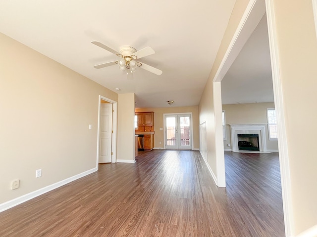 unfurnished living room featuring dark wood-style flooring, a fireplace with flush hearth, a ceiling fan, and baseboards