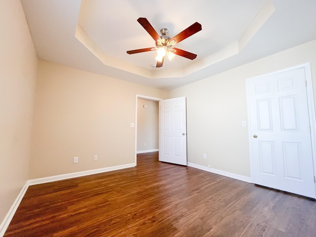 unfurnished room with dark wood-style floors, a raised ceiling, baseboards, and a ceiling fan