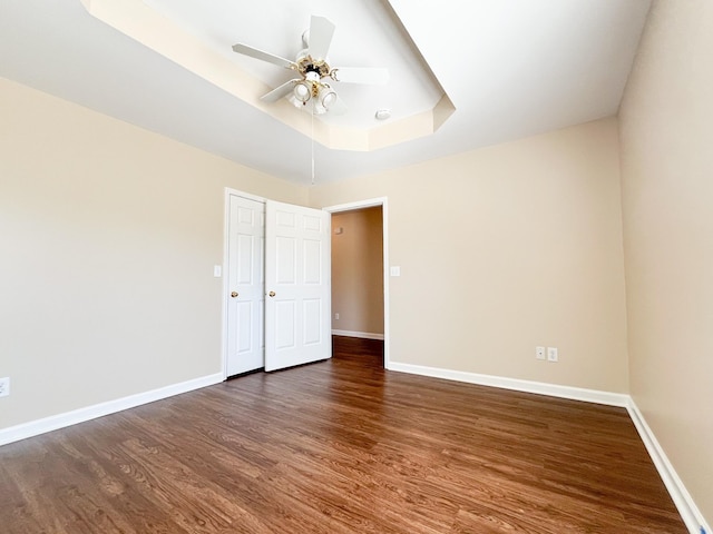 spare room with a ceiling fan, a raised ceiling, baseboards, and wood finished floors