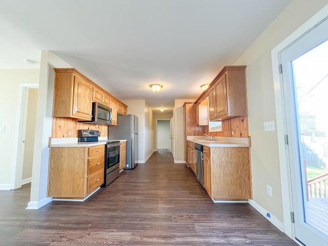 kitchen with light countertops, appliances with stainless steel finishes, a sink, and dark wood finished floors