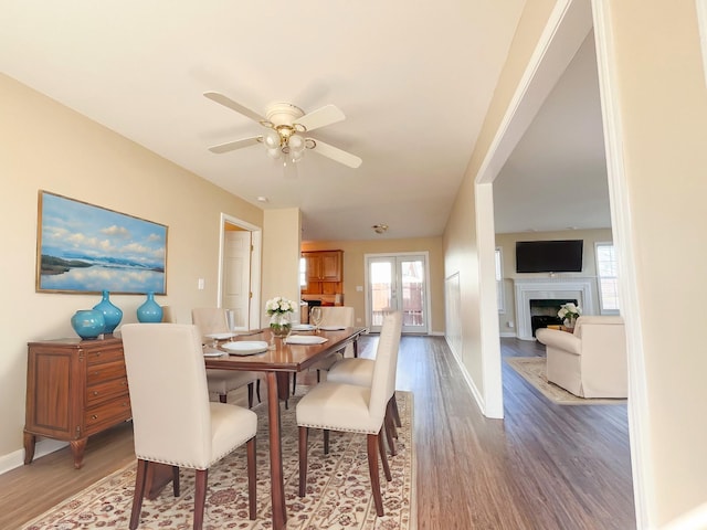 dining area with french doors, a fireplace, ceiling fan, wood finished floors, and baseboards