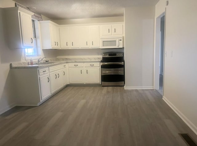 kitchen with white cabinets, white microwave, wood finished floors, stainless steel electric stove, and a sink