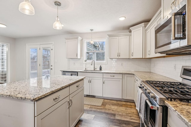 kitchen with wood finished floors, a sink, appliances with stainless steel finishes, light stone countertops, and pendant lighting