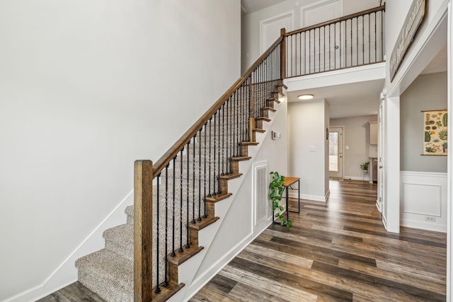 stairway featuring visible vents, baseboards, wood finished floors, a high ceiling, and a decorative wall