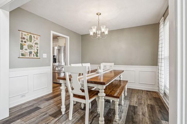 dining space with wainscoting, a notable chandelier, dark wood finished floors, and a decorative wall