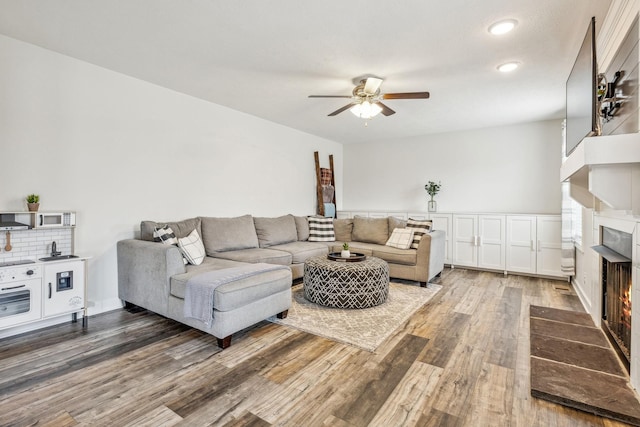 living room featuring ceiling fan, a lit fireplace, and wood finished floors