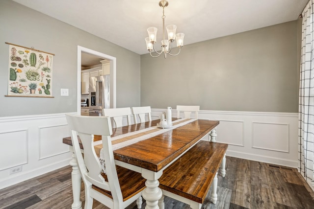 dining space featuring dark wood-style floors, a chandelier, a decorative wall, and wainscoting