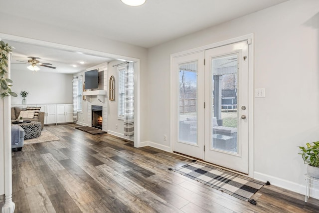 interior space with a ceiling fan, dark wood-style flooring, a large fireplace, and baseboards