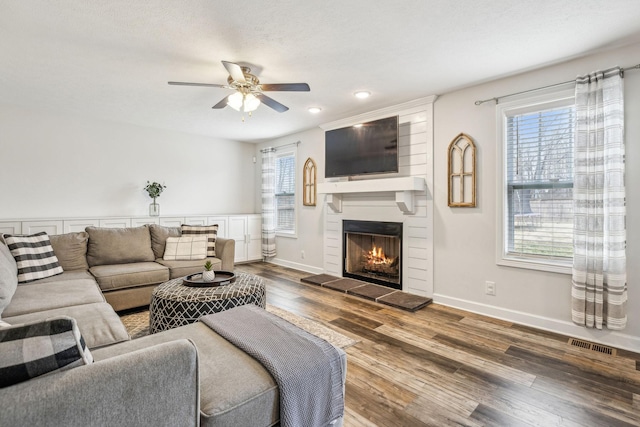 living room with visible vents, a large fireplace, ceiling fan, wood finished floors, and baseboards