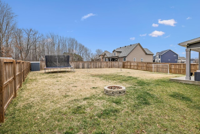 view of yard with a trampoline, central air condition unit, a patio area, a fenced backyard, and a fire pit