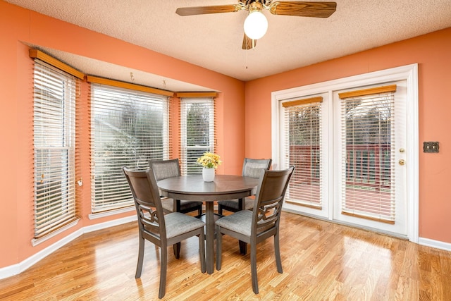 dining area featuring light wood-type flooring, ceiling fan, a textured ceiling, and baseboards