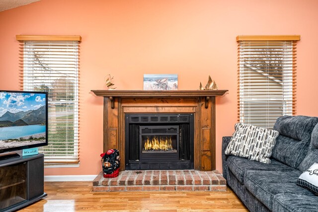 living area featuring vaulted ceiling, a glass covered fireplace, wood finished floors, and baseboards