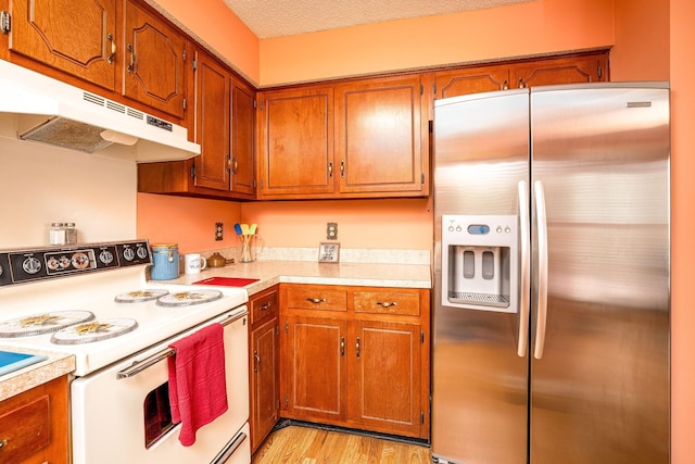 kitchen featuring stainless steel fridge, electric range, brown cabinetry, light countertops, and under cabinet range hood