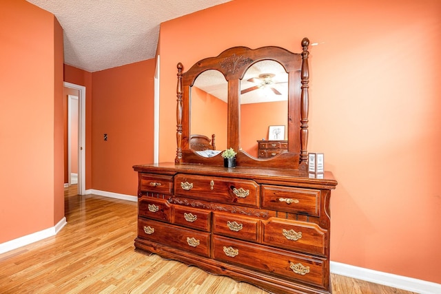 corridor featuring light wood-style flooring, baseboards, and a textured ceiling