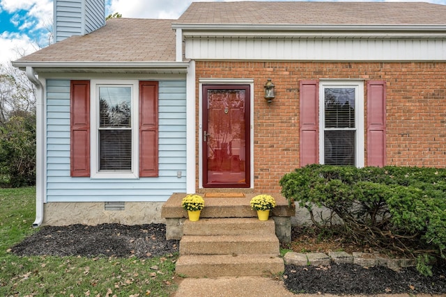 view of exterior entry featuring crawl space, roof with shingles, brick siding, and a chimney