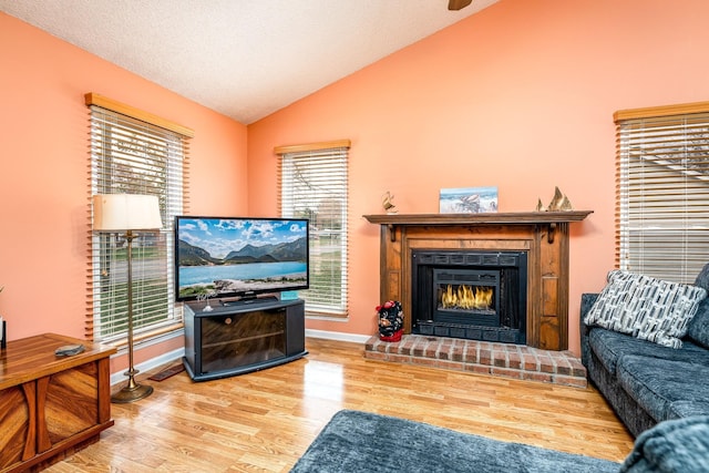 living room with a brick fireplace, vaulted ceiling, a textured ceiling, wood finished floors, and baseboards