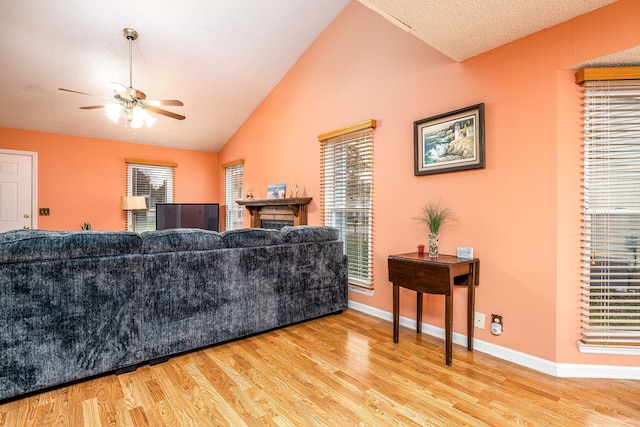 living room featuring a textured ceiling, a fireplace, baseboards, vaulted ceiling, and light wood-type flooring