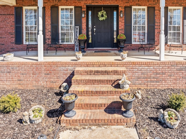 entrance to property featuring covered porch and brick siding