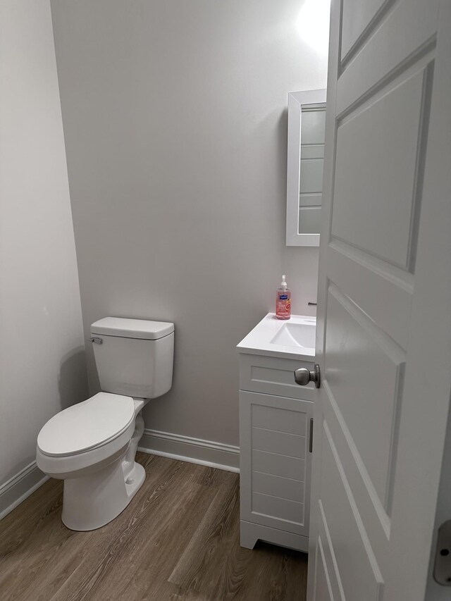 half bathroom with toilet, wood finished floors, vanity, and baseboards