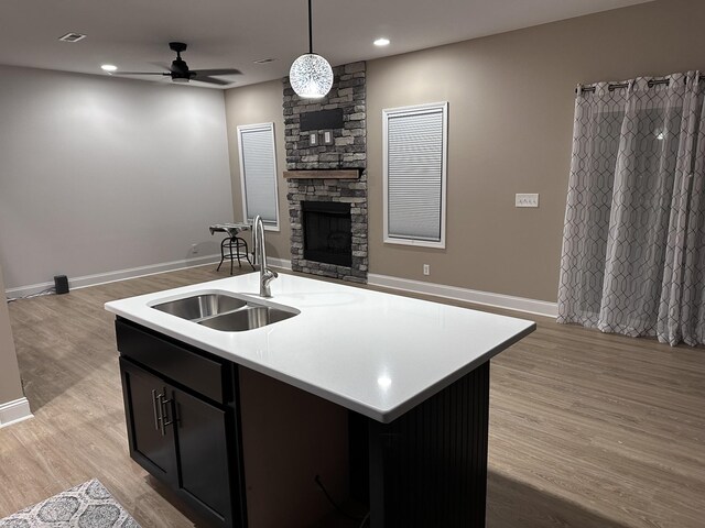 kitchen featuring a fireplace, light countertops, light wood-style flooring, open floor plan, and a sink