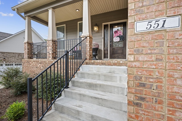 entrance to property featuring a porch and brick siding