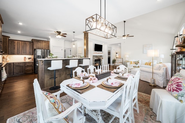 dining space with ceiling fan, dark wood-style flooring, vaulted ceiling, a fireplace, and recessed lighting